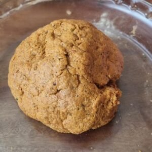 Chorizos veganos preparación paso 4: Agregar esta mezcla al gluten y amasar hasta que la masa este moldeable, si esta muy seca se le puede agregar un poco de agua y aceite. Masa color anaranjado dentro de una bowl de vidrio claro.