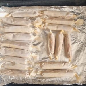 Chorizos veganos preparación paso 7: 18 porciones de nuestra masa de chorizos veganos envueltas como capsulas en papel pergamino (parchment) sobre una bandeja para hornear con papel platino.