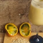 Receta de colada de avena o Quaker de naranjilla. Una copa con nuestra colada de avena, una naranjilla partida al lado izquierdo y unos granos de avena en la parte inferior.