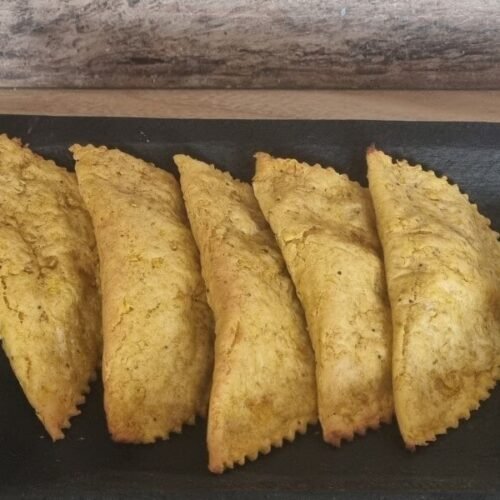 Empanadas veganas de plátano verde en una bandeja, al lado derecho un bowl con un aderezo de acompañamiento.
