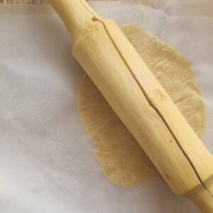 Paso número tres de la preparación de empanas veganas de plátano verde: Estirando la masa finamente con un bolillo sobre un papel cera.