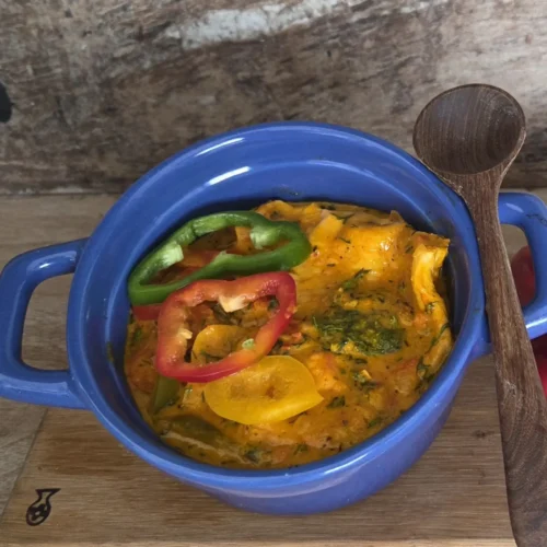 Plato final de moqueca vegana servido en una cazuela azul con asas, decorado con rodajas de pimientos y cilantro picado, acompañado de una cuchara de madera al lado.