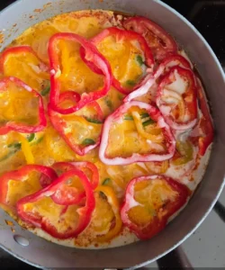 Moqueca brasileña de hongos hirviendo a fuego lento en una sartén, cubierta con rodajas de pimientos rojos y amarillos en una salsa cremosa de leche de coco.